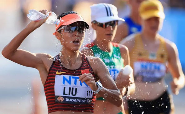 Female marathon runners pouring water over themselves during a race in extreme heat conditions.
