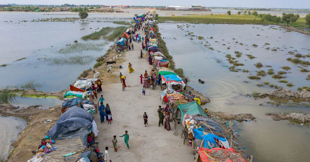 Flood-affected families setting up temporary shelters along a road surrounded by water.