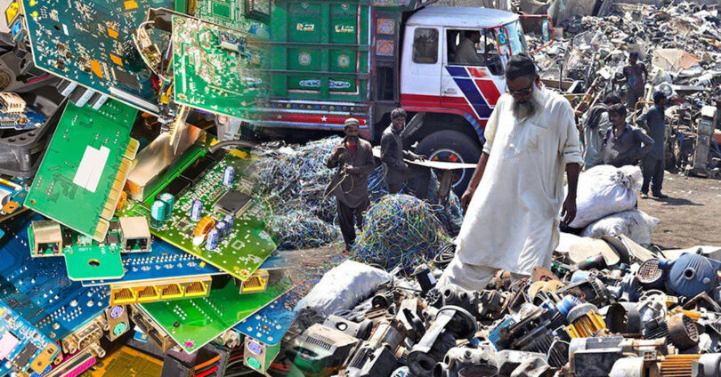 Workers sorting electronic scrap and wires in an open scrapyard surrounded by piles of discarded equipment and debris.