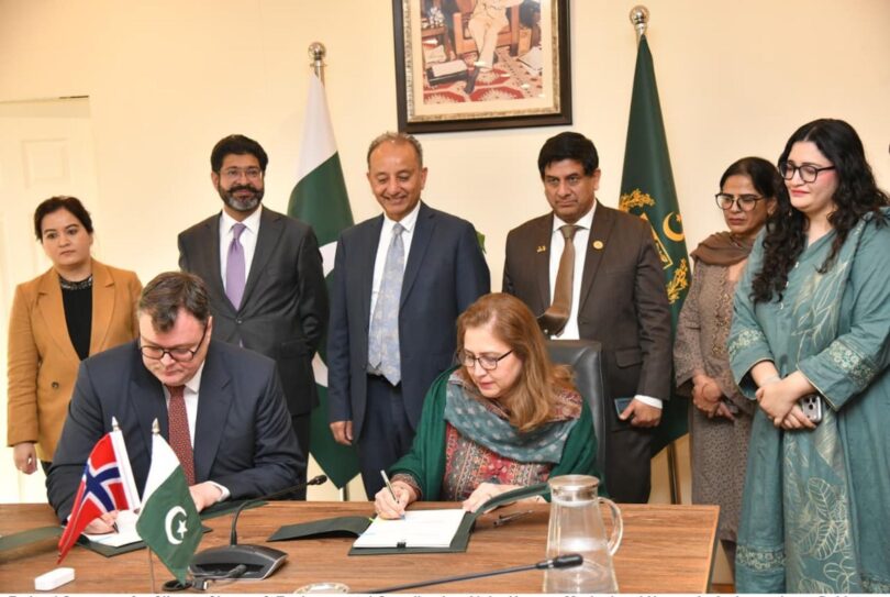 Officials from Pakistan and Norway sign a bilateral climate agreement under Article 6.2 of the Paris Agreement during a formal ceremony in Islamabad, with representatives standing behind and national flags displayed.